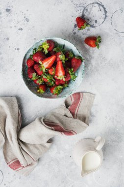 Eski seramik kasede taze çilek ve gri beton arka planda yeşil yapraklar. Sağlıklı kahvaltı konsepti. Üst görünüm.