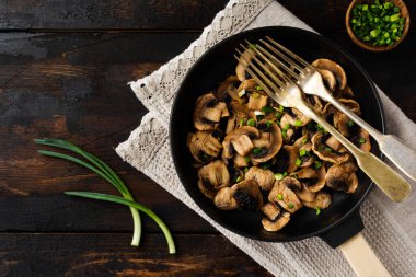 Kızarmış Champignon mantarları eski, siyah ahşap bir arka planda, dökme demir bir tavada kızartılmak üzere. Üst görünüm.