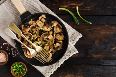 Kızarmış Champignon mantarları eski, siyah ahşap bir arka planda, dökme demir bir tavada kızartılmak üzere. Üst görünüm.