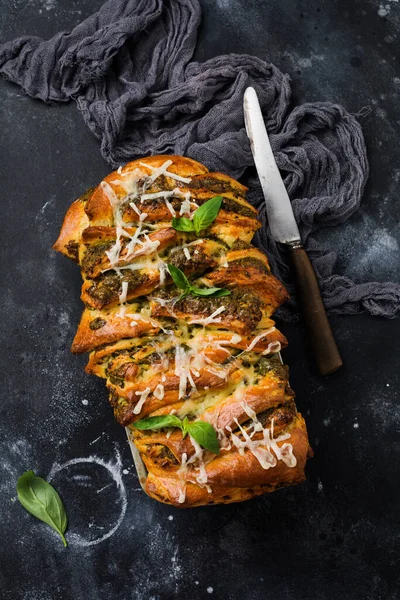 Pull-apart bread with Italian pasta pesto, basil and parmesan cheese in baking form over old dark concrete background. Top view. Rustic stile.