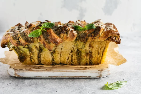 Pull-apart bread with Italian pasta pesto, basil and parmesan cheese in baking form over old light concrete background. Top view. Rustic stile.