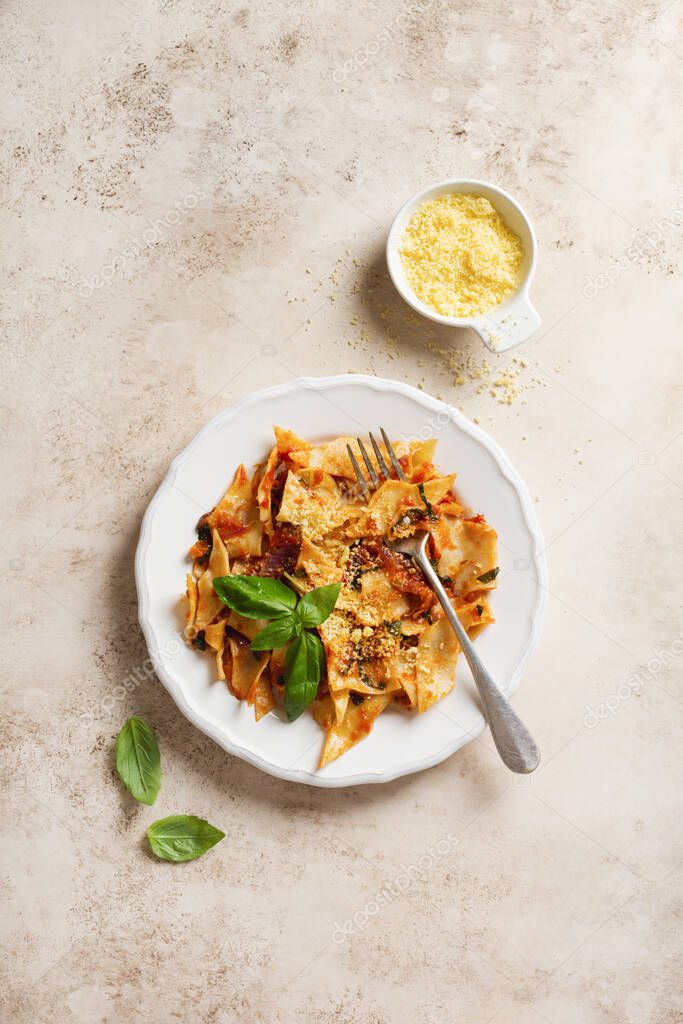 Pasta Maltagliati with classic tomato sauce, parmesan and basil on a rustic concrete light table background. Traditional Italian dish serving. Top view.