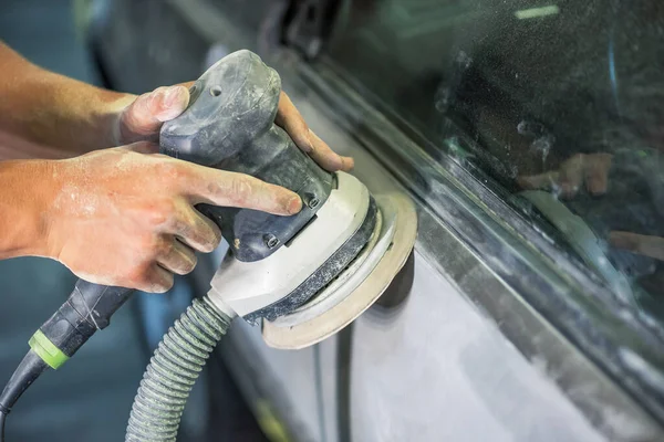 Grinder in the hands of a man who sharpen a car varnish in the car shop.