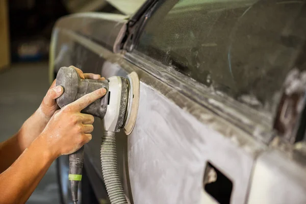 Grinder in the hands of a man who sharpen a car varnish in the car shop.