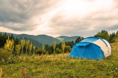 Çimen tarlasında kamp manzarası. Ormanın arka planı, dağlar ve doğal parktaki günbatımı gökyüzü..