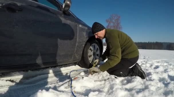 Een man montage van sneeuwkettingen. — Stockvideo