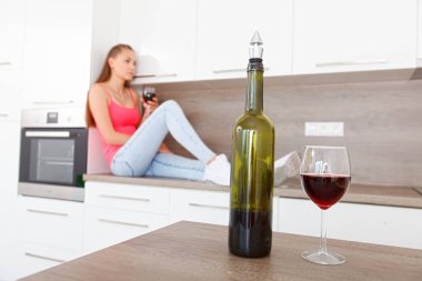 Genç kadın alkol sorunları çözer. Alkol bağımlılığı. Şarap ön planda, arka planda bir kadın odaklanmak kasıtlı olarak bulanık. (Renk tonlu görüntü).