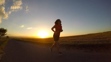 Gün batımında koşmak. Yaz öğleden sonra egzersiz yapan genç bir kadın..