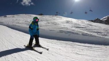 Küçük bir çocuk kayak yapıyor. 6 yaşında bir çocuk Alp tatil beldesinde kış tatilinin tadını çıkarıyor. Sabit görüntü. Yavaş çekim.