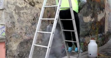 Boyalı bir duvardan duvar yazısını silmek. İşçi boyalı duvarı spreylerden temizler..