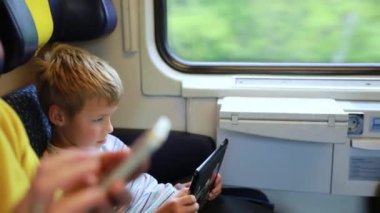 Genç bir kadın oğlunuzla birlikte trenle seyahat ediyor. Genç bir kadın elektronik bir kitap okuyup tablet üzerinde çalışıyor..