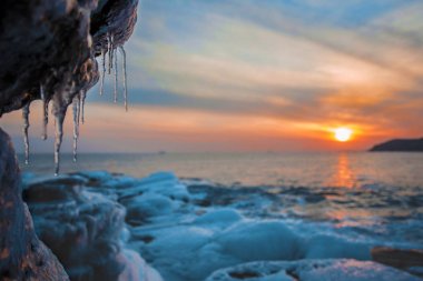İçinde ön ve bulanık bir arka plan üzerinde buz sarkıtları ile günbatımı kışın buzlu deniz kıyısı