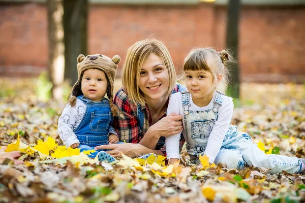 Jovem mãe com crianças pequenas encontra-se nas folhas amarelas . — Fotografia de Stock