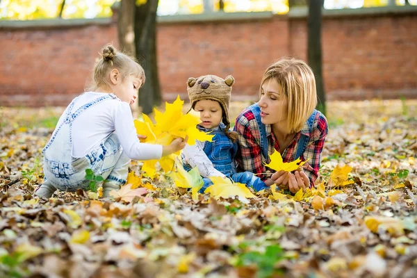 Junge Mutter mit kleinen Kindern liegt in den gelben Blättern. — Stockfoto