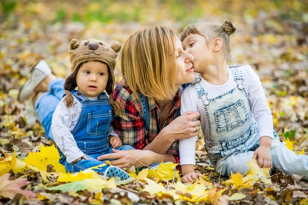 Junge Mutter mit kleinen Kindern liegt in den gelben Blättern. — Stockfoto