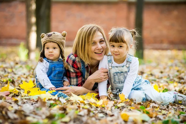 Young mother with young children lies in the yellow leaves. — Stockfoto