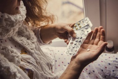 Genç bir kız hastalandı ve elinde haplarla pencerenin kenarında oturuyordu. Hasta kadın elinde hap tutuyor..