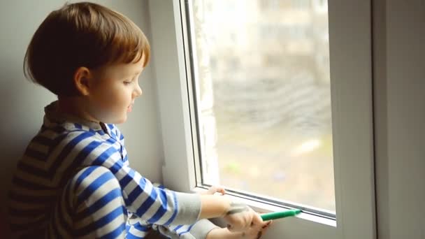 Kleiner Junge zeichnet eine Markierung am Fenster, Fensterbank — Stockvideo