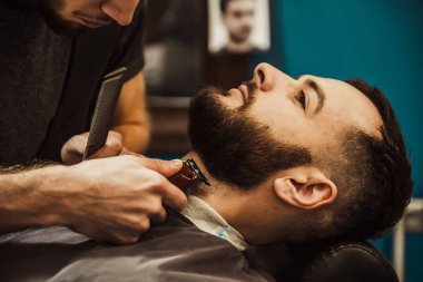 Berber kuaföründe hippi jileti olan bir adama sakal kesiyor..