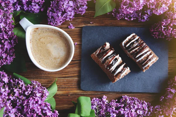 A lilac, a cake and a cappuccino are on the table.