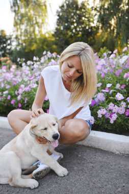 Bir sarışın bir Labrador köpek yavrusu ile oynuyor.