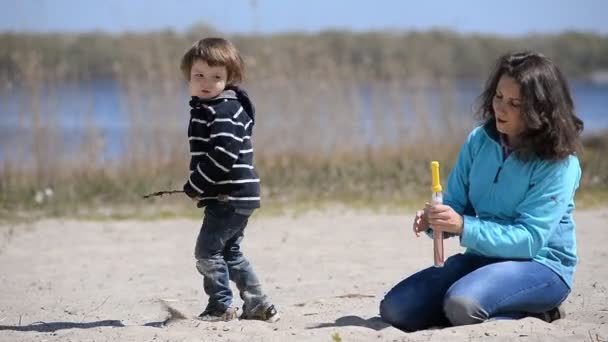 Enfant avec maman jouant des bulles de savon sur la plage — Video