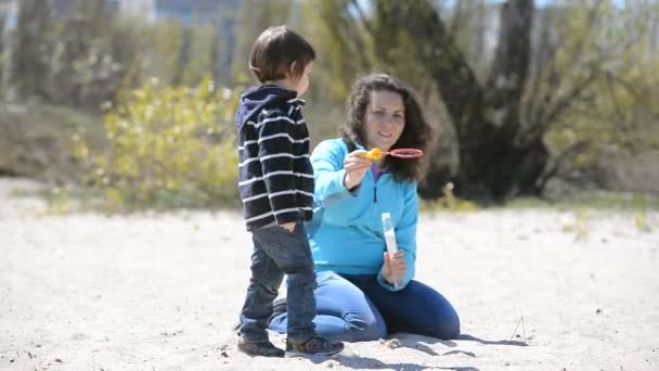 Kind mit Mama spielt Seifenblasen am Strand — Stockvideo