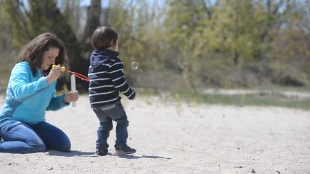 Kluk s mámou hrát mýdlové bubliny na pláži — Stock video