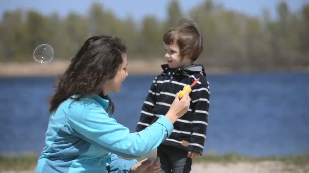 Niño con mamá jugando burbujas de jabón en la playa — Vídeos de Stock