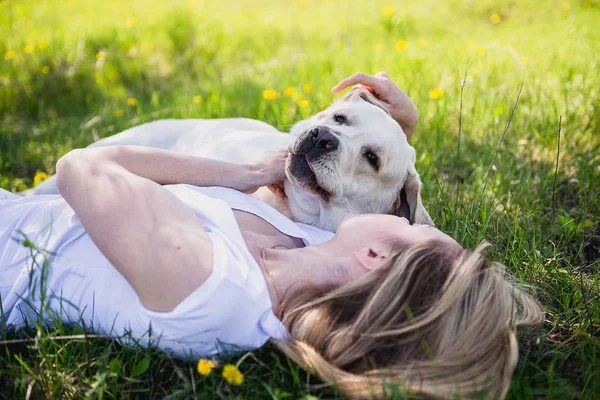 Tjejen ligger på gräset och kramar hund labrador — Stockfoto