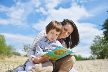 Sahilde bir kitap okuma bir toddler kadınla.