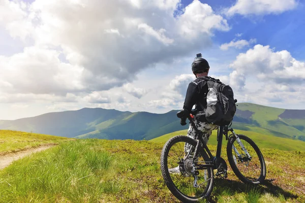 Un joven se para con una bicicleta en la cima de una montaña — Foto de Stock