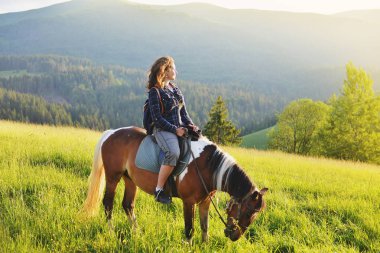 Bir kadın dağlarda at üstünde oturuyor