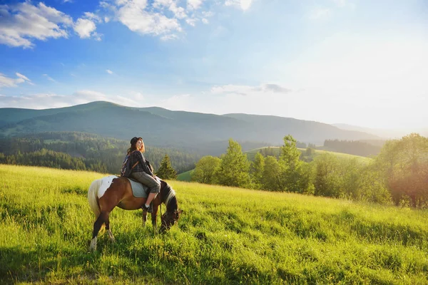 A woman is sitting on a horse in the mountains