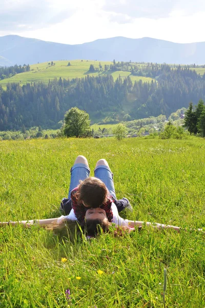 Žena s malým synem leží na trávě v horách. Cesta do hor. — Stock fotografie
