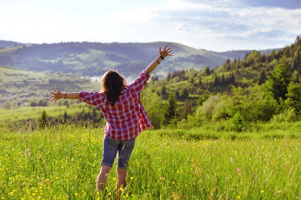 The girl raised her hands and stands on a meadow in the mountains in the summer — Stock Photo, Image