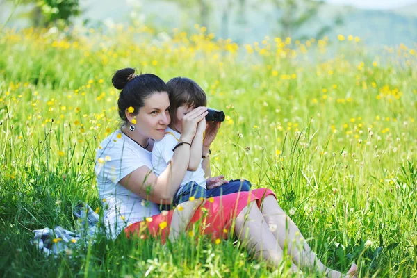 Mutter mit ihrem kleinen Sohn, der durch ein Fernglas auf dem Gras in den Bergen sitzt — Stockfoto