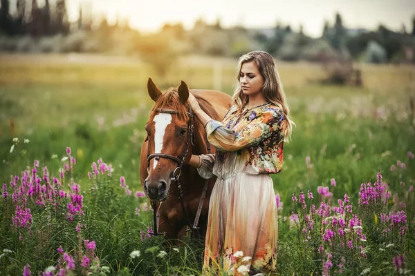 Jeune femme se tient près d'un cheval dans une robe d'été sur une prairie — Photo