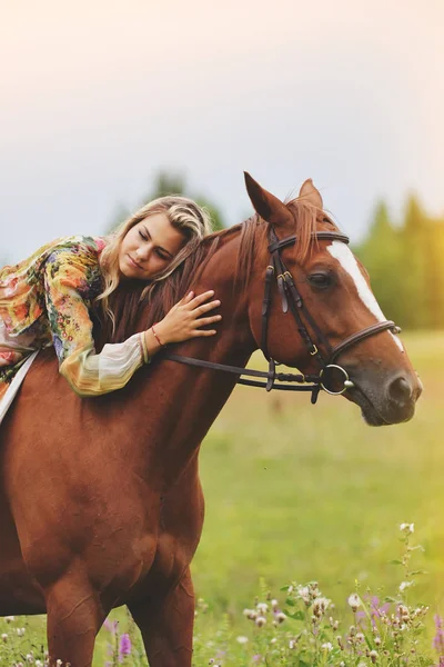Mujer joven se sienta en un caballo en un prado de verano — Foto de Stock