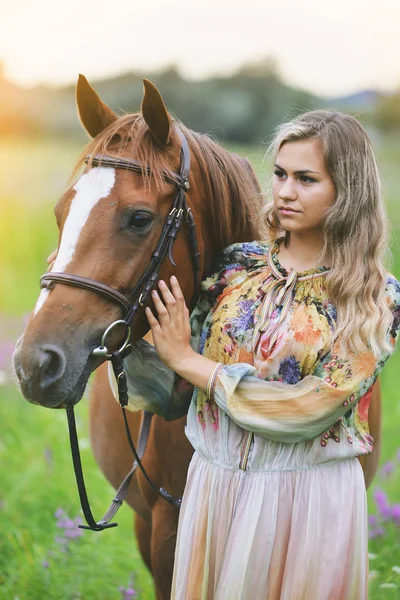 Jovem mulher fica perto de um cavalo em um vestido de verão em um prado — Fotografia de Stock