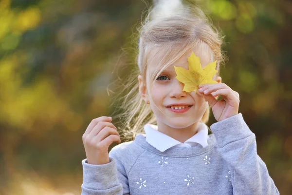 Bambina che gioca con foglie gialle nel parco autunnale — Foto Stock