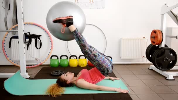Νεαρή γυναίκα να κάνει ασκήσεις με μια μεγάλη μπάλα στο γυμναστήριο. — Αρχείο Βίντεο