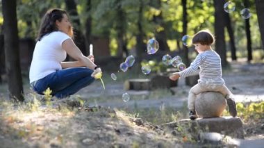 Küçük bir çocuk ve onun anne parkta yürüyor. Sabun balonları anne darbeler.
