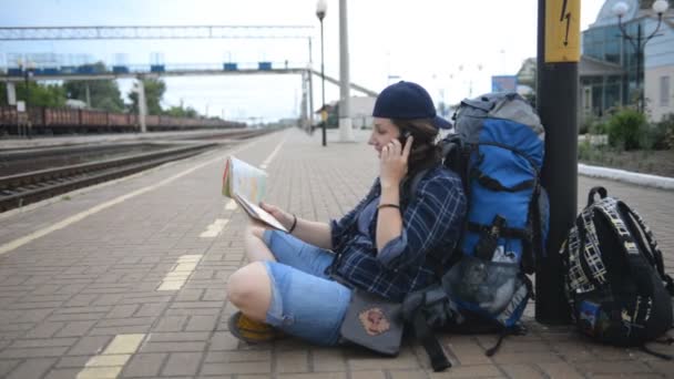 Junge Frau sitzt auf dem Bahnsteig im Bahnhof und schaut auf die Karte — Stockvideo