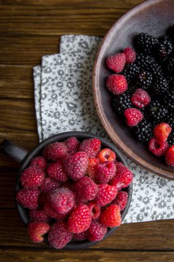 Seramik mug ahududu ile ve böğürtlen ile bir kase üzerinde ahşap bir masa standı.