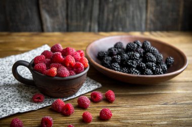 Seramik mug ahududu ile ve böğürtlen ile bir kase üzerinde ahşap bir masa standı.