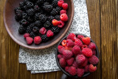 Seramik mug ahududu ile ve böğürtlen ile bir kase üzerinde ahşap bir masa standı.