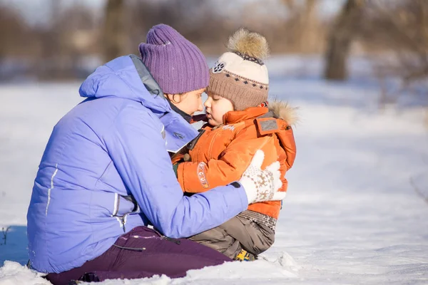 Mulher com pequeno filho brincando no parque no inverno na neve . — Fotografia de Stock