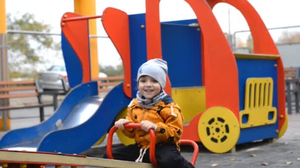 O garoto está montando em um balanço no playground . — Vídeo de Stock