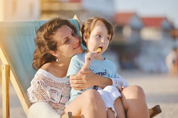 Junge Frau mit Baby sitzt im Stuhl am Sommerstrand. — Stockfoto